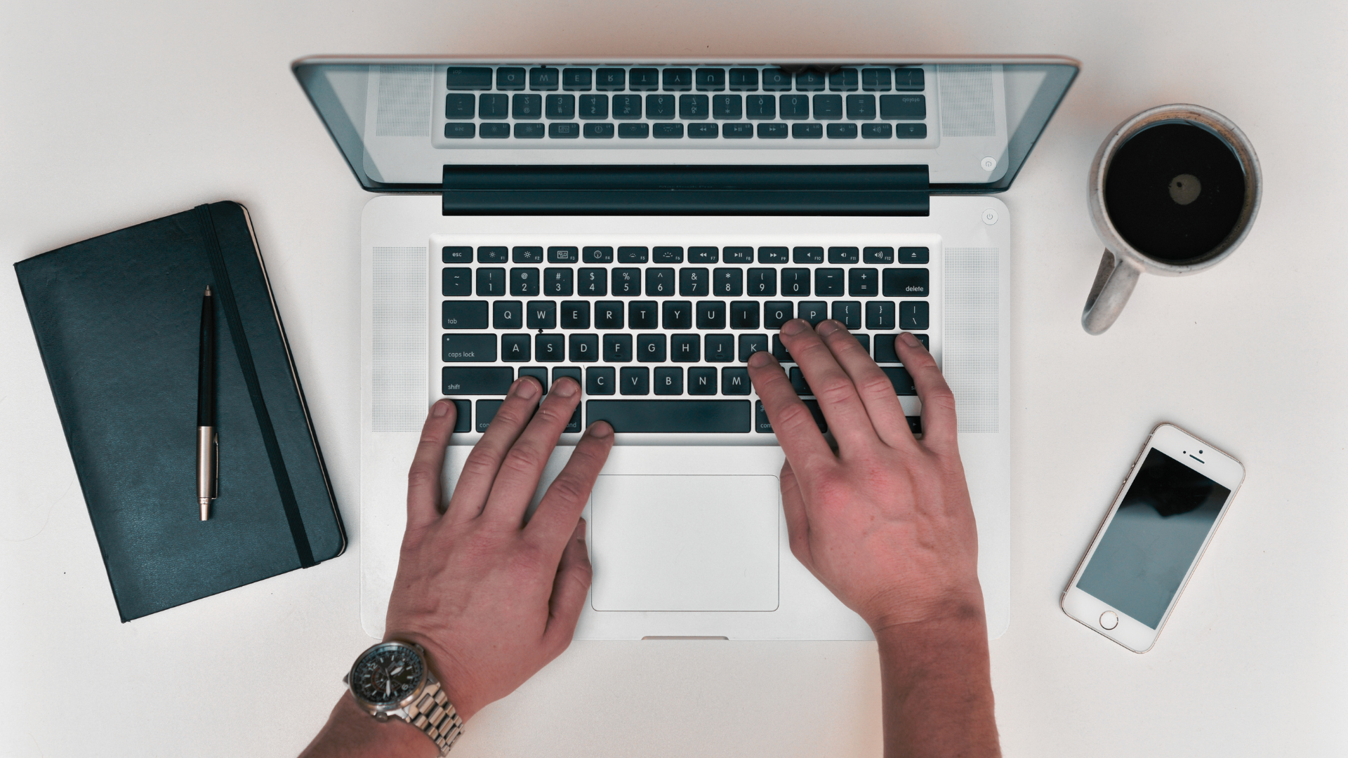 Overhead view of hands typing on a laptop with notebook and coffee